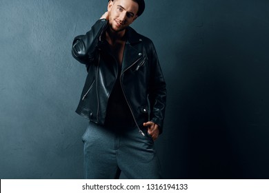 Attractive Young Man In A Jacket Holds His Hand Behind His Neck And A Black Leather Jacket A Gray Background     