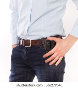 Attractive Young Man In Jeans And Shirt Putting Cell Phone In Front Pocket, Against White Background