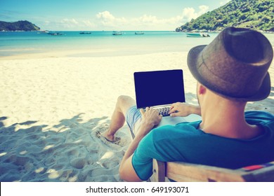 Attractive Young Man With Laptop Working On The Beach. Freedom, Remote Work, Freelancer, Technology, Internet, Travel And Vacation Concepts