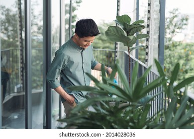 Attractive Young Man On Apartment Balcony Watering Plants In Box From Blue Watering Can