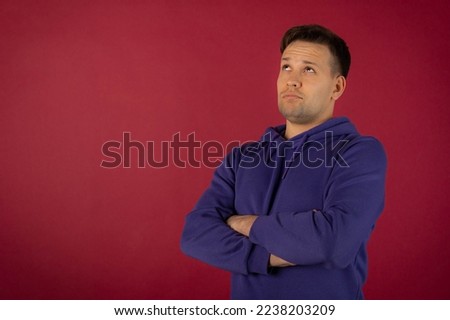 Attractive young man in a purple sweatshirt on a red background is thinking about something, not smiling, brown eyes