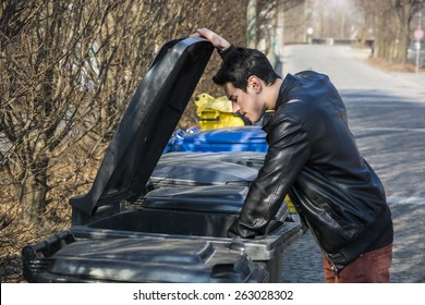 Attractive Young Man Putting Out Rubbish Standing With The Lid Up On A Bin In A Row Of Garbage Bins At The Side Of A Street