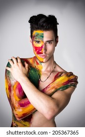 Attractive young man shirtless, skin painted all over with bright Holi colors on light background