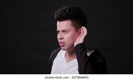 An attractive young man showing an I can't hear gesture against a black background. Close-up Shot