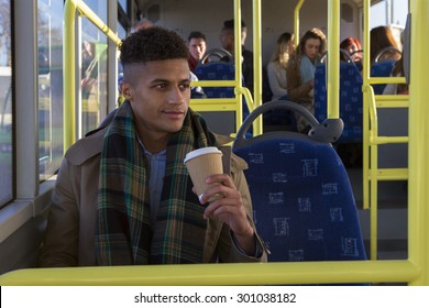 Attractive young man sitting on the bus with a cup of coffee. He is looking out the window and is smiling.