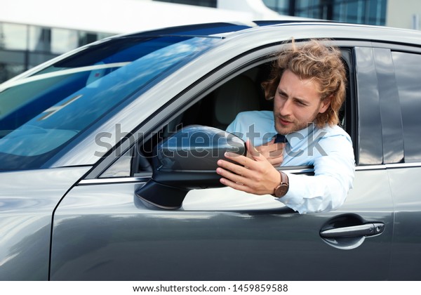 Attractive\
young man straightens tie in his luxury\
car