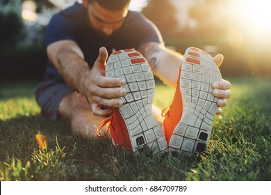Attractive young man stretching in the park before running at the sunset focus on shoes - Shutterstock ID 684709789