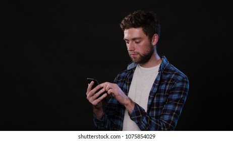 An attractive young man using a phone against a black background. Medium Shot