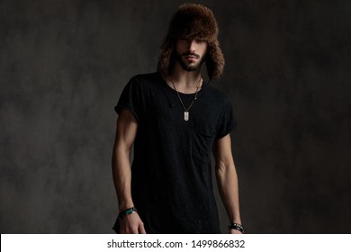 attractive young man wearing a fur hat, standing isolated on grey background