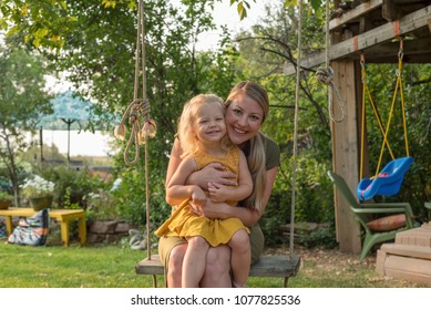 Attractive Young Mom And Daughter On A Swing Playing In The Backyard On A Summer Day