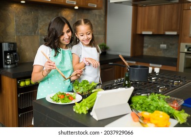 Attractive Young Mom And Little Girl Making An Online Video Call On A Tablet While Cooking Dinner Together