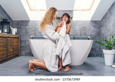 Attractive young mother with light curly hair in bathroom dressing gown kneeling and wiping with white towel her little handsome son. - Powered by Shutterstock