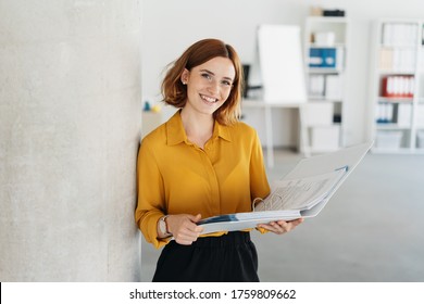 Attraktive junge Büroangestellte, die einen großen offenen Buchbinder hält, während sie die Kamera mit einem süßen freundlichen Lächeln anschaut