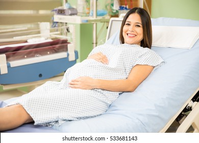 Attractive Young Pregnant Woman Waiting In A Hospital Bed Before Going Into Labor And Smiling