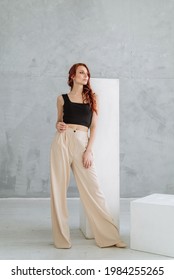 An Attractive Young Red-haired Woman In A Black Tank Top And Wide White Stylish Trousers. Slim Female Model In Pants, Casual Style