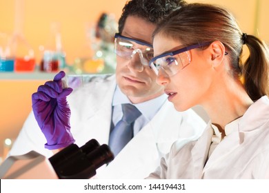 Attractive young scientist and her supervisor looking at the microscope slide in the forensic laboratory.