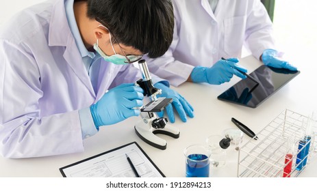 Attractive Young Scientist Team In Lab Coat And Safety Goggles Working With Analysing Test Trial Or Investigations With Test Tubes In Laboratory