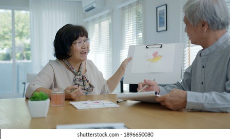 Attractive young senior asian citizen couple sit at home watercolor painting artwork on desk table feeling happy in mental health therapy or asia older people quarantine activity lifestyle concept.