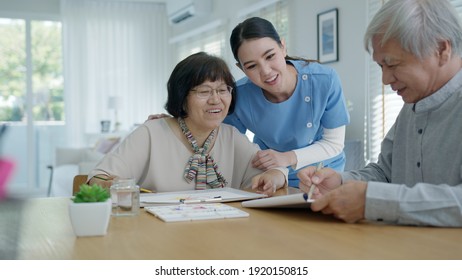 Attractive Young Senior Asian Citizen Couple Sit At Home Watercolor Painting Artwork On Desk Table With Nurse Feeling Happy In Mental Health Therapy Or Asia Older People Quarantine Activity Lifestyle.