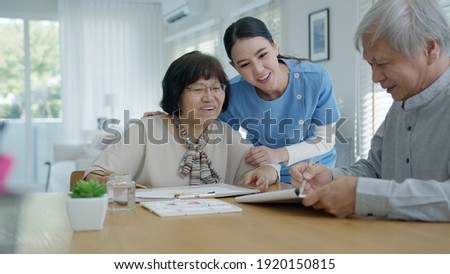 Attractive young senior asian citizen couple sit at home watercolor painting artwork on desk table with nurse feeling happy in mental health therapy or asia older people quarantine activity lifestyle.