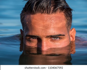 Attractive Young Shirtless Athletic Man Standing In Water In Sea Or Lake, With Half Face Submerged Underwater, Looking At Camera