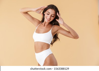 Attractive young slim girl posing in swimwear isolated over beige background, eyes closed