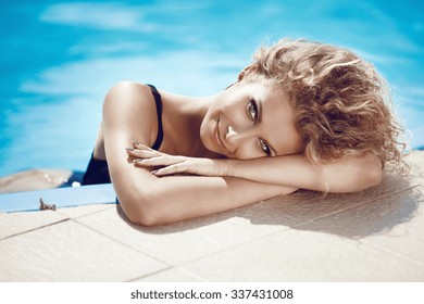 Attractive Young Smiling Girl Model Sunbathing And Tanned In Blue Swimming Pool On Summer Vacation. Healthy Body Care. 