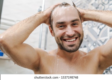 Attractive Young Smiling Man Washing Hair While Standing In The Shower