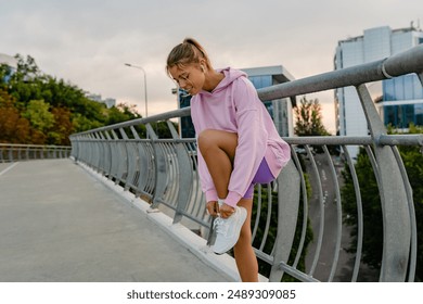 attractive young smiling woman in stylish sportswear in pink hoodie and sneakers doing sports in morning outdoors, stretching, healthy lifestyle, skinny strong body - Powered by Shutterstock