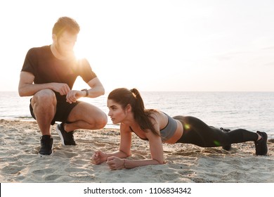 Attractive young sport couple doing plank exercise at the beach - Powered by Shutterstock