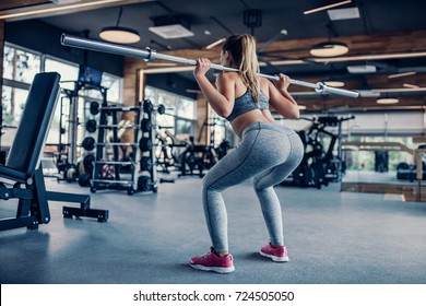 Attractive young sports woman with barbell. Doing squats. Back view of beautiful girl squatting.