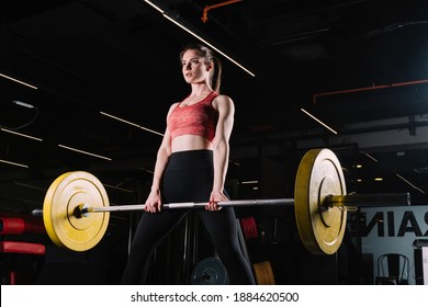 Attractive young sports woman doing deadlift with barbell. Crossfit and fitness. Beautiful young fitness woman exercising with heavy dumbbell in dark gym studio. Deadlift bodybuilding fitness workout.