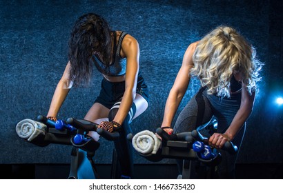 Attractive young sporty women riding indoor bikes during cycling class indoors.