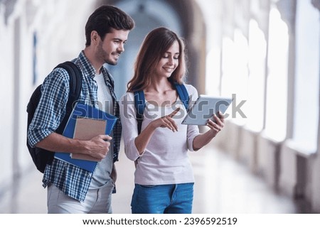 Attractive young students are using a digital tablet and smiling while standing in university hall