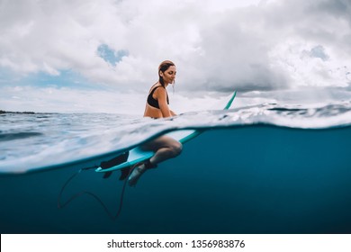 Attractive young surf girl sit at surfboard in blue ocean - Powered by Shutterstock