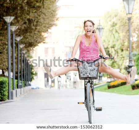 Attractive young tourist woman visiting a destination city and riding a bike in a wide avenue, stretching her legs and having a fun and excitement expression, outdoors.