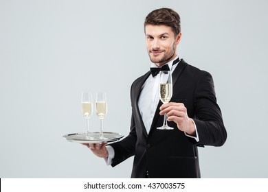 Attractive young waiter in tuxedo holding tray and glass of champagne over white background - Powered by Shutterstock