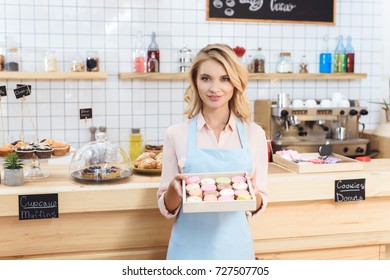 attractive young waitress holding box with cookies and smiling at camera - Powered by Shutterstock