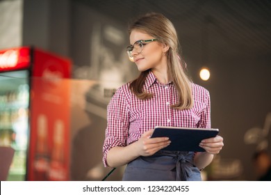 Attractive young waitress using a tablet computer to take an order from a customer in a coffee shop