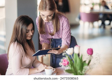 Attractive young waitress using a tablet computer to take an order from a customer in a coffee shop
