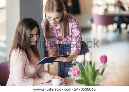 Attractive young waitress using a tablet computer to take an order from a customer in a coffee shop