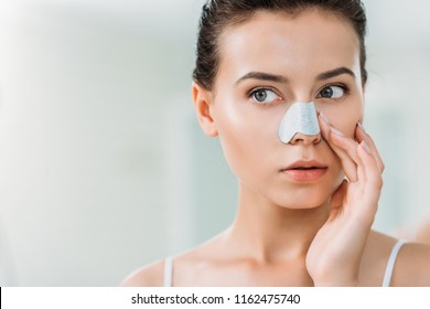 attractive young woman applying nose strip in bathroom 