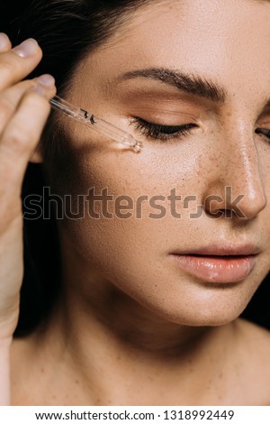 attractive young woman applying serum on face with pipette