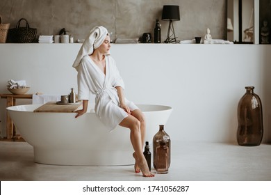 Attraktive junge Frau im Bademantel sitzend am Rande der Badewanne.