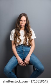 Attractive young woman in blue jeans a T-shirt, sitting in a slouched position with a provocative attitude