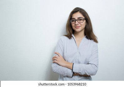 Attractive young woman, brunette, wearing glasses and a business light shirt on a white background. Portrait of a successful Indian girl with arms crossed on her chest.