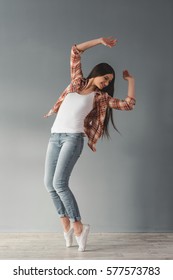 Attractive young woman in casual clothes is smiling while standing on her toes, on gray background