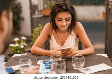 Attractive young woman in casual summer attire using smartphone at an outdoor cafe table. Modern lifestyle scene showcasing mobile technology use, social media engagement - casual dining experience. - Powered by Shutterstock