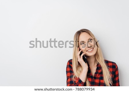 Attractive young woman chatting on her mobile phone listening to the conversation with a smile of pleasure over a white background studio with copy space