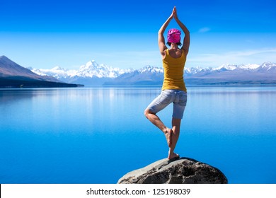 An Attractive Young Woman Doing A Yoga Pose For Balance And Stretching Near The Lake  High In The Mountains